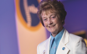 A woman with short hair and a white jacket standing smiling 